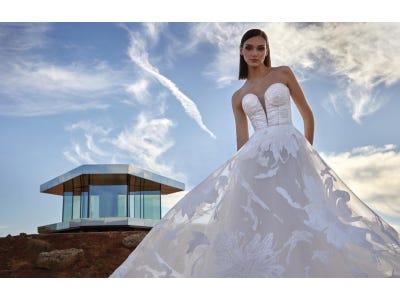 Noiva posando junto a um edifício usando um vestido princesa com transparências e bordados conjugados com um corpete