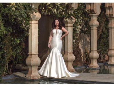 Jeune femme portant une robe de mariée grande taille bustier coupe sirène, dans un décor extérieur somptueux