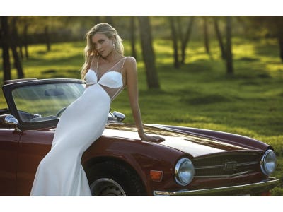 Mujer vesta de novia en una boda en un jardín sobre un coche rojo 