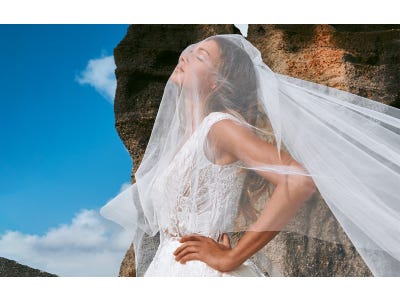 Mujer al aire libre vestida de novia con los ojos cerrando con un velo de novia cayéndole por la cara
