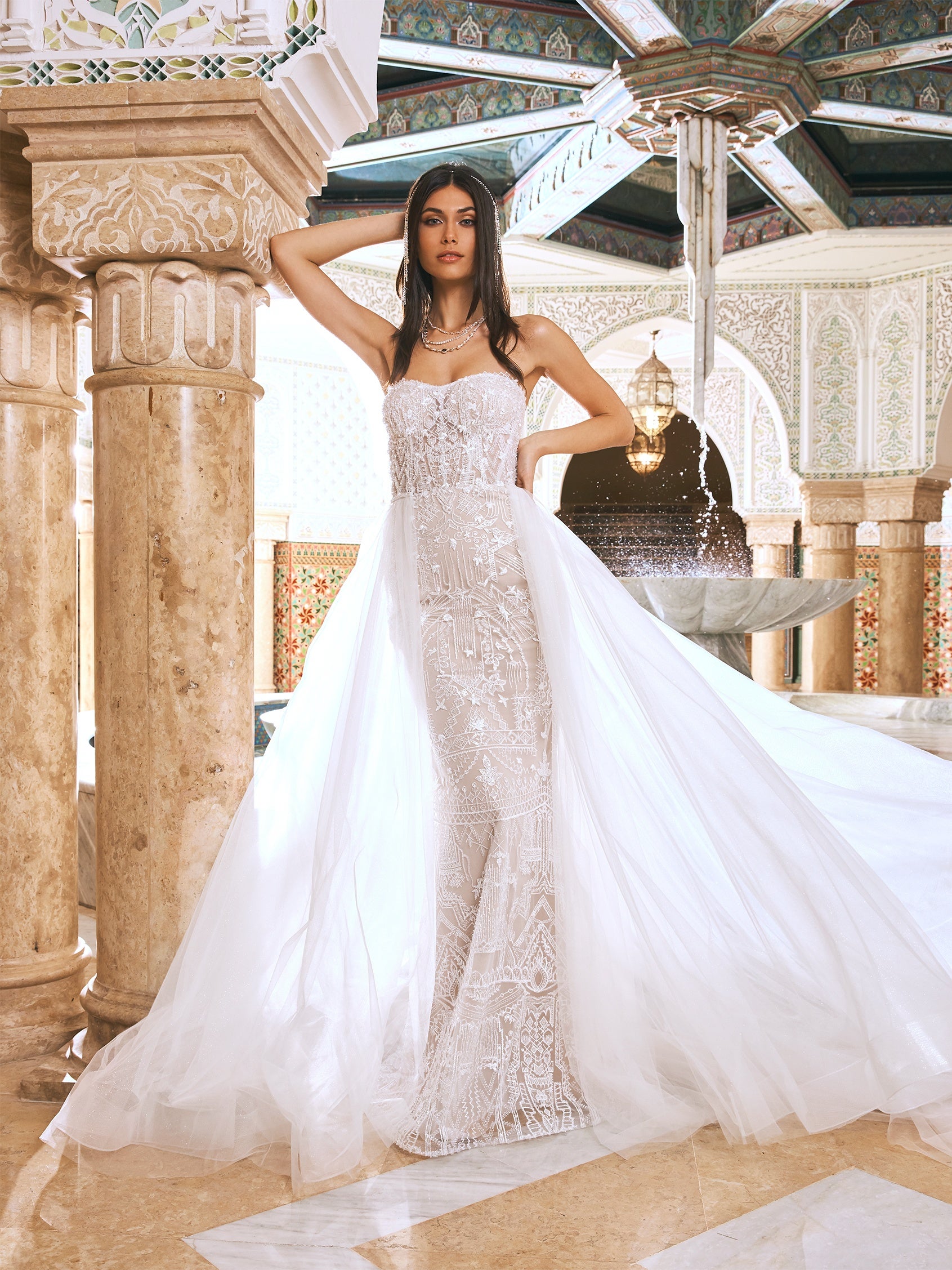 Ein in den 1920er Jahren inspiriertes Brautkleid mit ausgestelltem Rock aus handgefertigter Spitze fließt sanft über Rücken und Gesäß und wird durch eine prächtige Kapellenschleppe aus butterweichem Tüll abgerundet. Der Überrock sorgt für zusätzliches Volumen, damit der Gang zum Altar ein ganz besonderer Auftritt wird. 