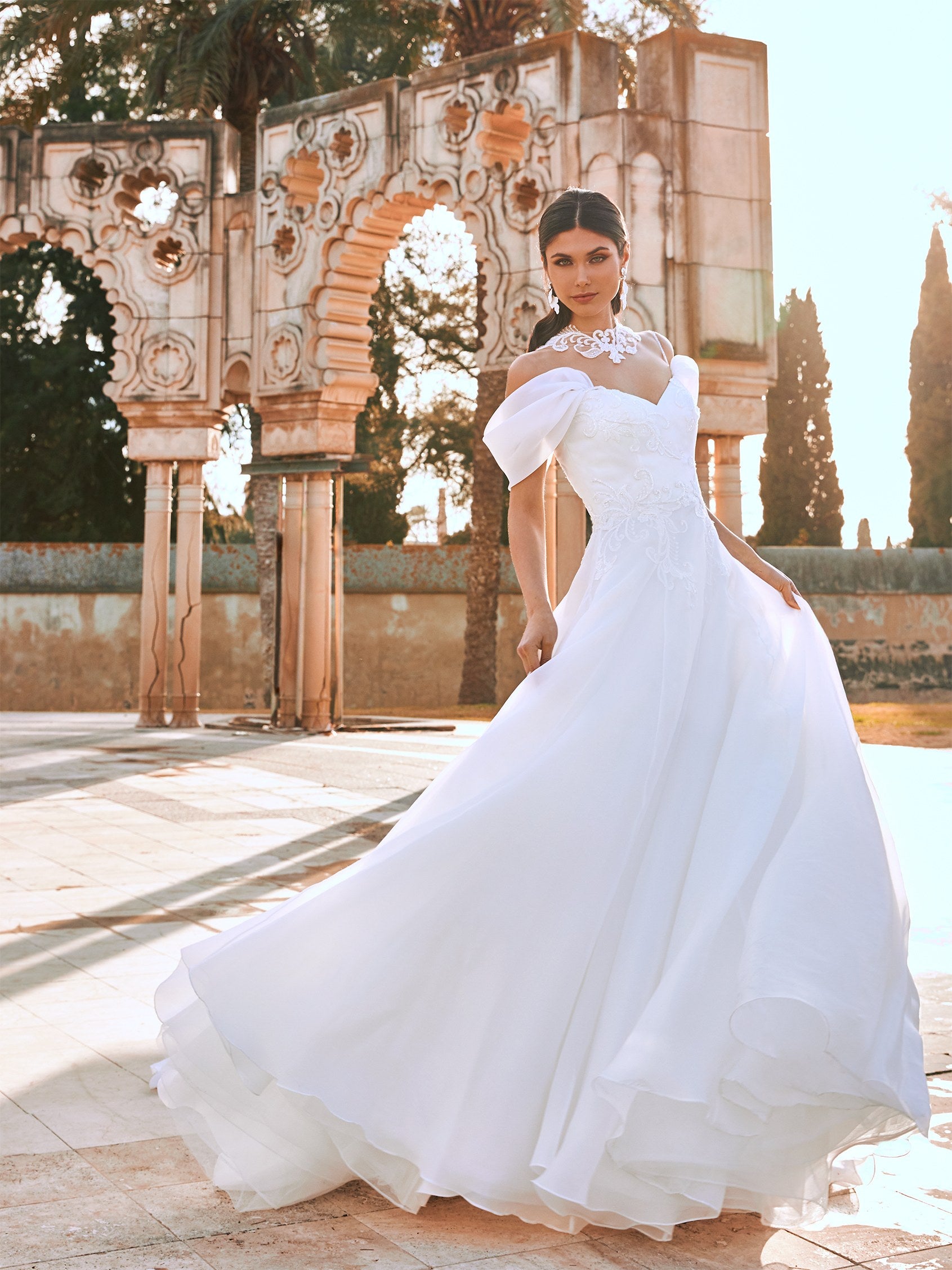 Die perfekte Ballkleid-Silhouette wird zum ultimativen Hochzeitskleid. Mit einem perfekt geformten, trägerlosen Oberteil, sinnlicher Peek-a-Boo-Spitze auf dem Rücken, einem bestickten Tüllrock und einer Schleppe, die einer Königin angemessen ist. 