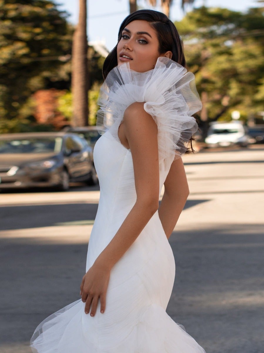 Weniger ist mehr bei diesem makellos geschnittenem Kleid im Meerjungfraustil aus glänzender Mikadoseide. Das asymmetrische Dekolleté betont feminine Schultern und verleiht dem Kleid einen trendigen Touch. Ideal für alle modernen Bräute. 
