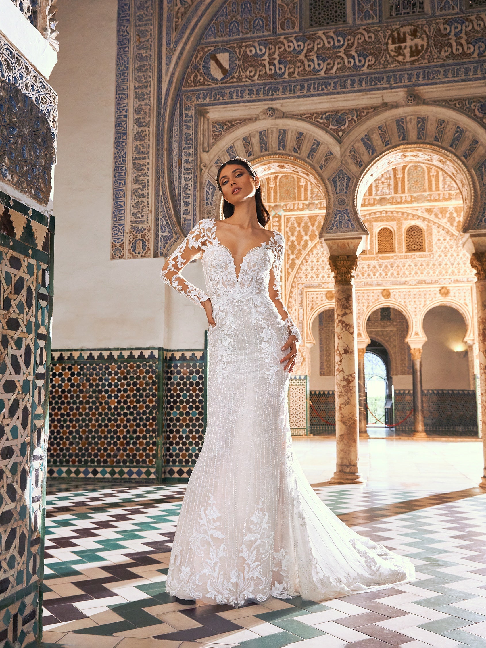 Ein in den 1920er Jahren inspiriertes Brautkleid mit ausgestelltem Rock aus handgefertigter Spitze fließt sanft über Rücken und Gesäß und wird durch eine prächtige Kapellenschleppe aus butterweichem Tüll abgerundet. Der Überrock sorgt für zusätzliches Volumen, damit der Gang zum Altar ein ganz besonderer Auftritt wird. 