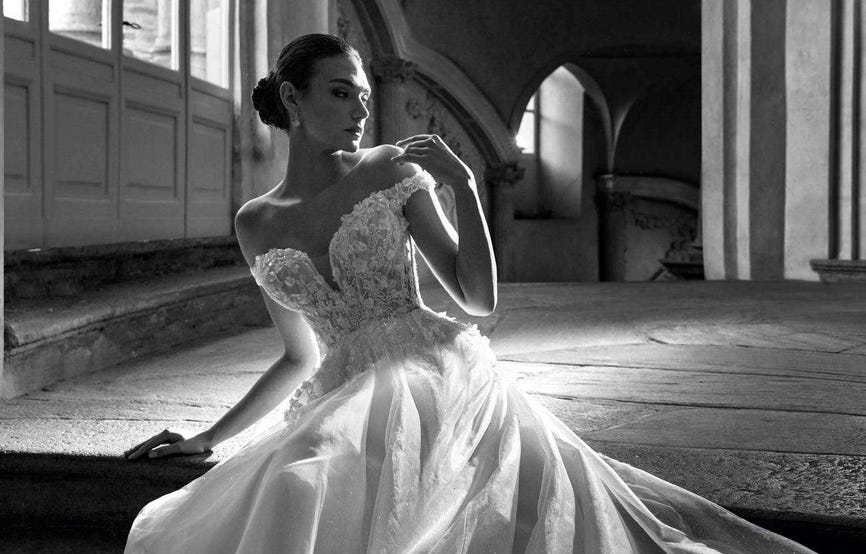 Mujer sentada en unas escaleras de piedra llevando un vestido de novia de princesa real mirando hacia un lado