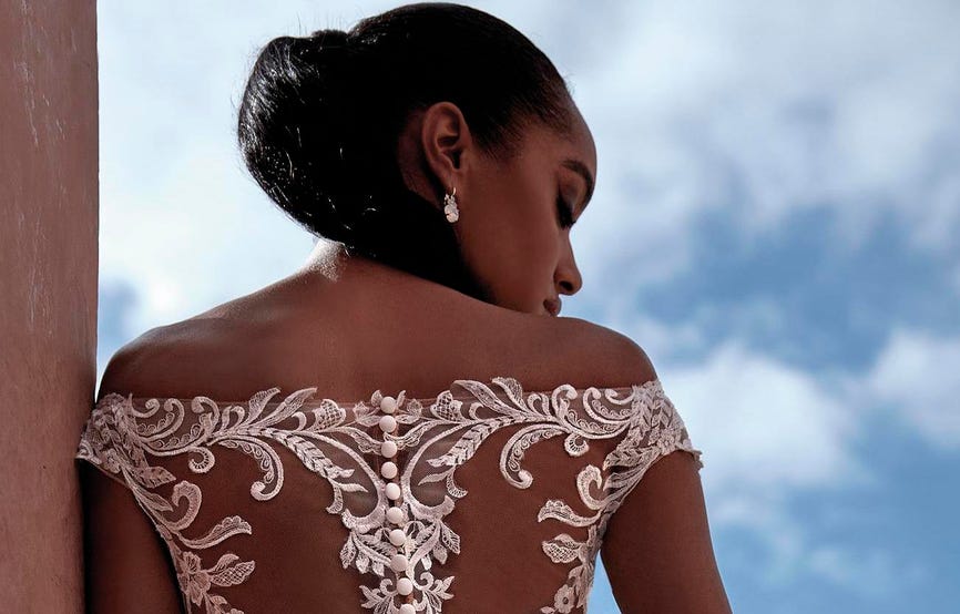 Mujer de espaldas con un vestido de novia con transparencias en la espalda y con una coleta mirando de lado