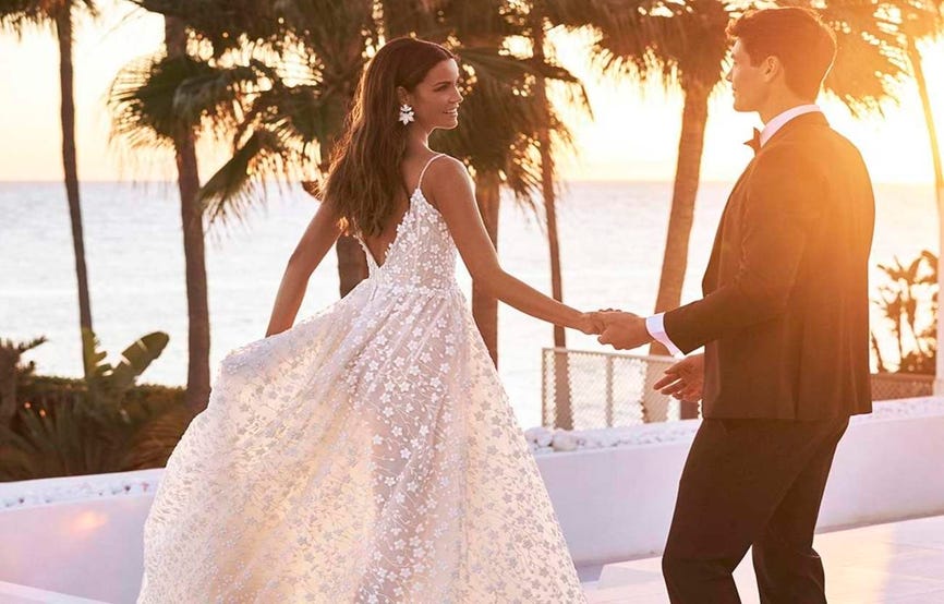 Un couple de mariés se tenant la main au coucher du soleil sur une plage. Une scène romantique et idyllique.