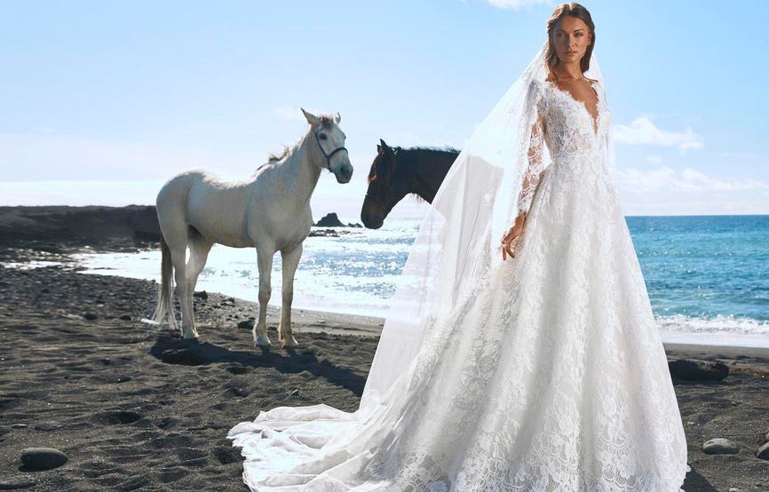 Mujer con vestido de novia en la playa frente a dos caballos