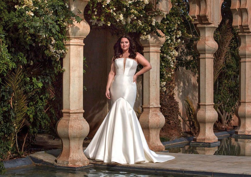 Jeune femme portant une robe de mariée grande taille bustier coupe sirène, dans un décor extérieur somptueux
