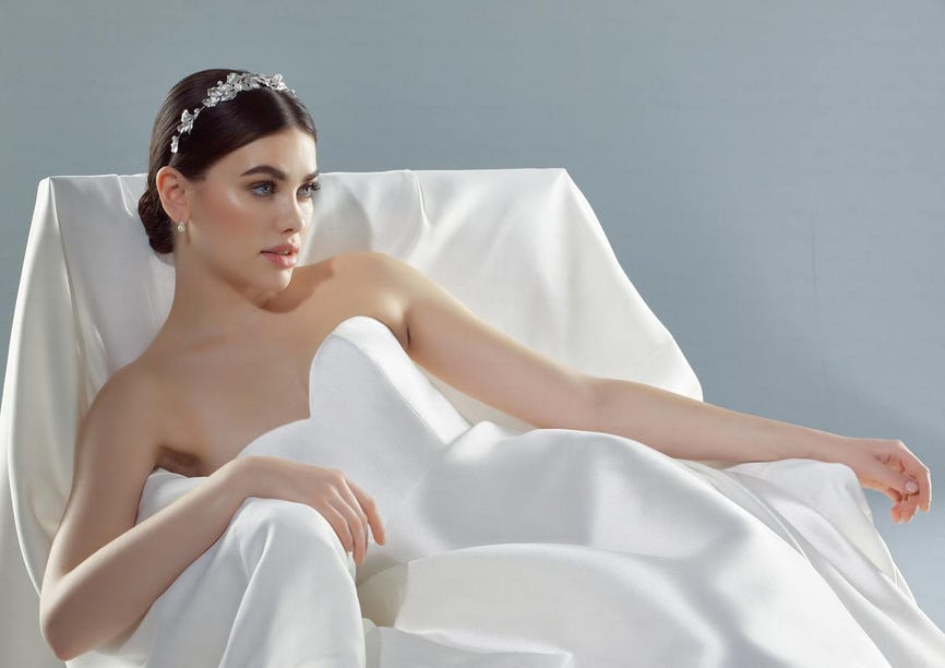 Femme élégante, dans une robe de mariée bustier blanche repose gracieusement sur un canapé blanc, exhibant son vernis pastel.