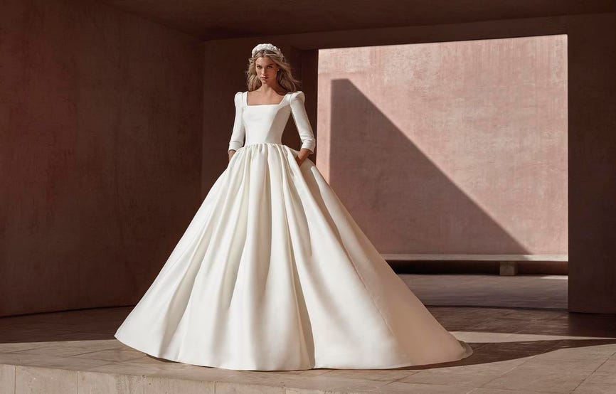 Woman with blonde hair in a long-sleeved, ball gown wedding dress with a square neckline in satin.