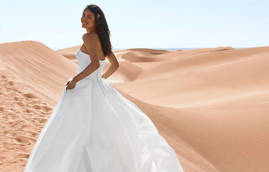 Woman with dark hair in a simple strapless wedding dress in a princess style cut standing in sand dunes. 