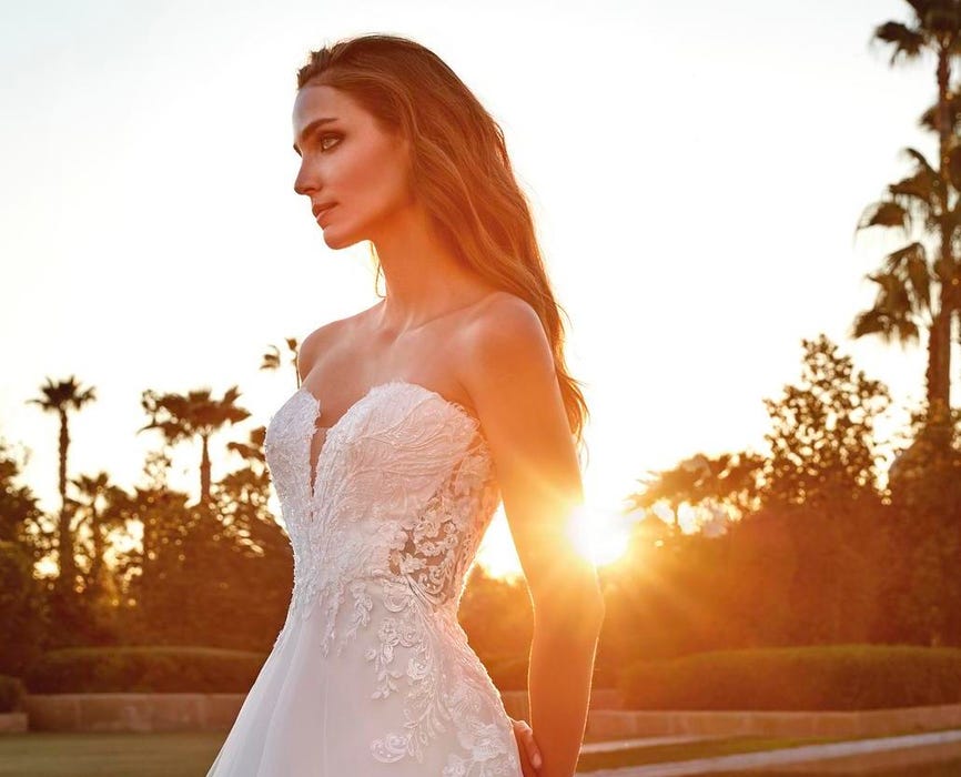 Brunette woman wearing a strapless wedding dress with lace detailing, sheer back, and sweetheart neckline. 