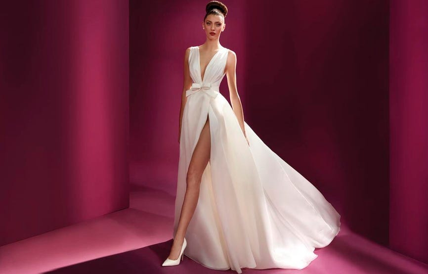 Modella che indossa un lungo abito da sposa con scollo a V, spacco laterale e scarpe décolleté da sposa bianche. 