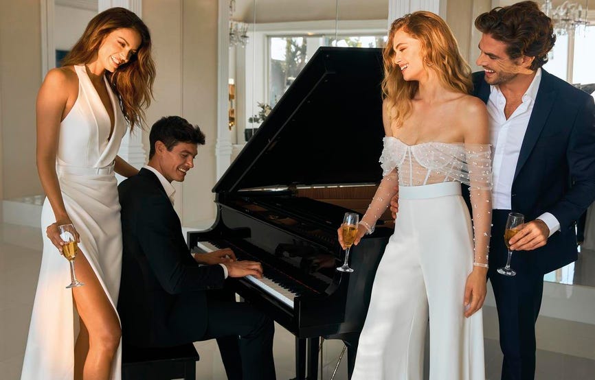 Una boda con un vestido de novia con pantalón en casa celebrando. Dos novias y dos novios frente a un piano.