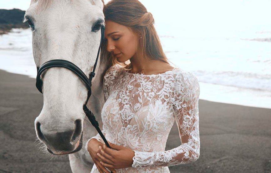 Mujer vestida de novia junto a un caballo en la playa