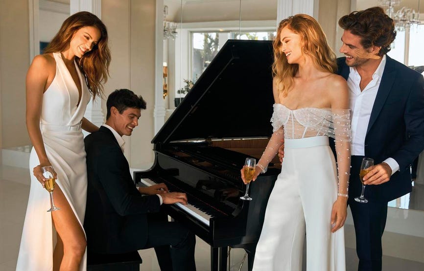 Casamiento civil en el que hay dos mujeres vestidas de blanco y dos hombre con traje en una casa tocando el piano y brindando