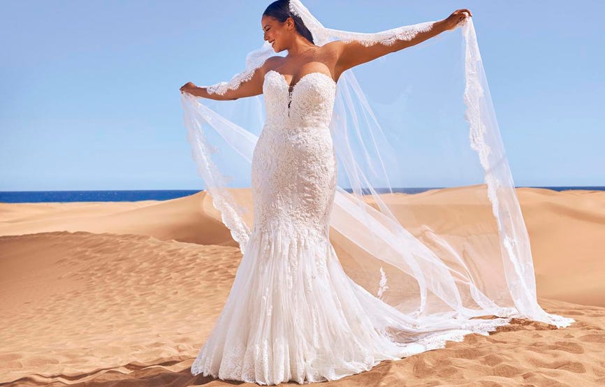 Mujer sobre arena de desierto vestida de novia de tallas grandes con un velo y vestido corte sirena con encaje