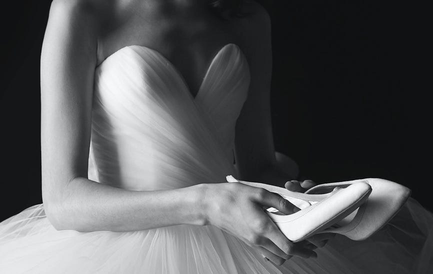 Brazos de una mujer que lleva un vestido de novia sujetando los zapatos para el vestido de novia