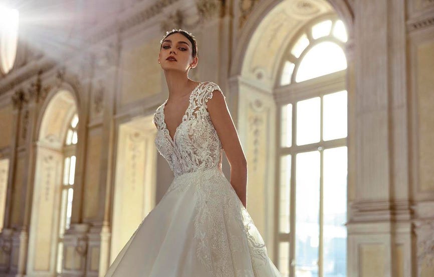 Woman in a V-neck princess wedding dress with a lace bridal overskirt and a jewelled headpiece. 