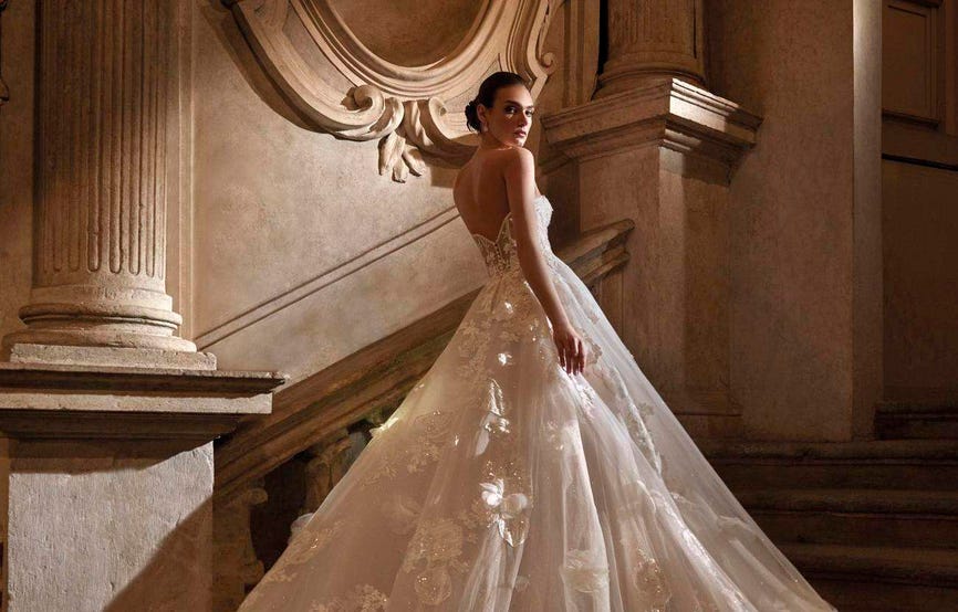 Woman wearing a princess A-line bridal dress with V-back and a flowing tulle skirt, going up a staircase in a ballroom