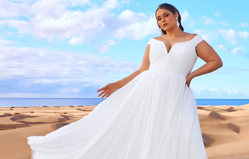 Mujer en la playa con el cielo azul de fondo llevando un vestido de novia plus size.