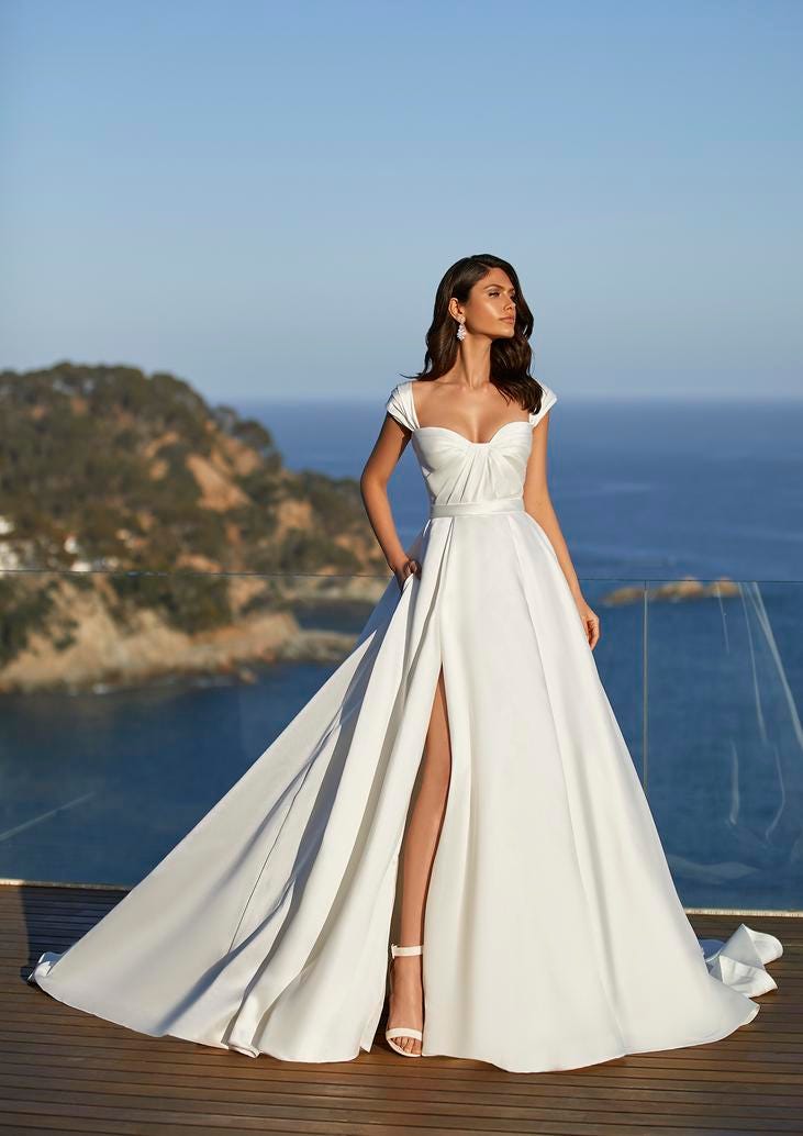 Dark-haired woman wearing a princess wedding dress with a slit and white bridal heels.