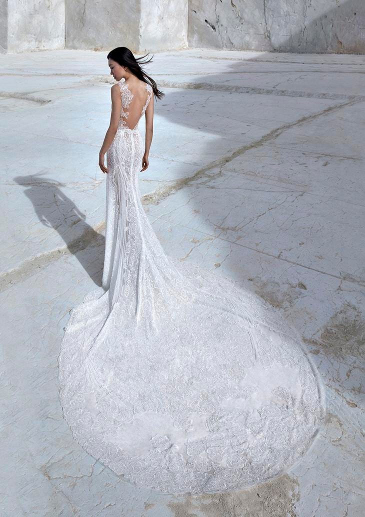 Modella di schiena con abito da sposa a sirena con strascico lungo, schiena scoperta e dettagli in pizzo.