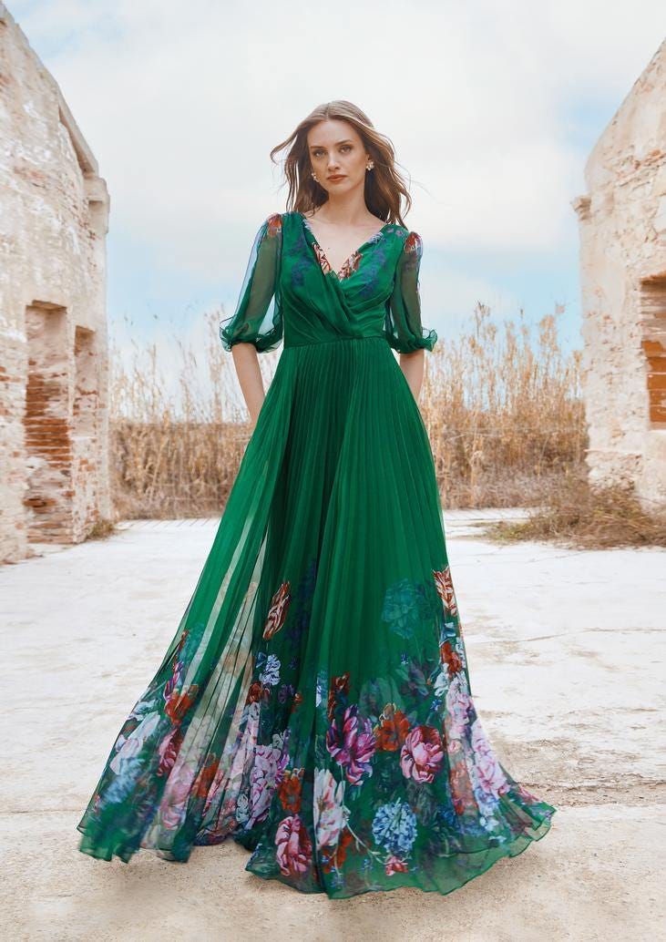 Donna che cammina con abito da damigella A line morbido verde smeraldo con scollo a cuore e fantasia di fiori sulla gonna. 