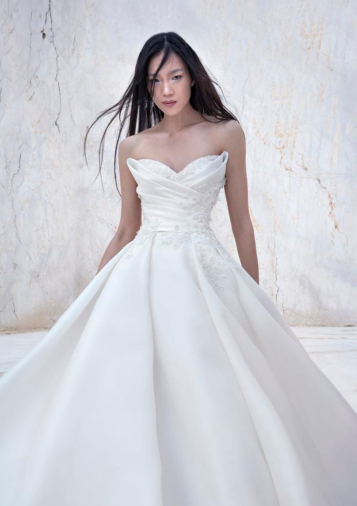 Jeune femme vêtue d'une robe de mariée blanche bustier princesse. Robe dotée d'un drapé et d'élégants motifs en dentelle.