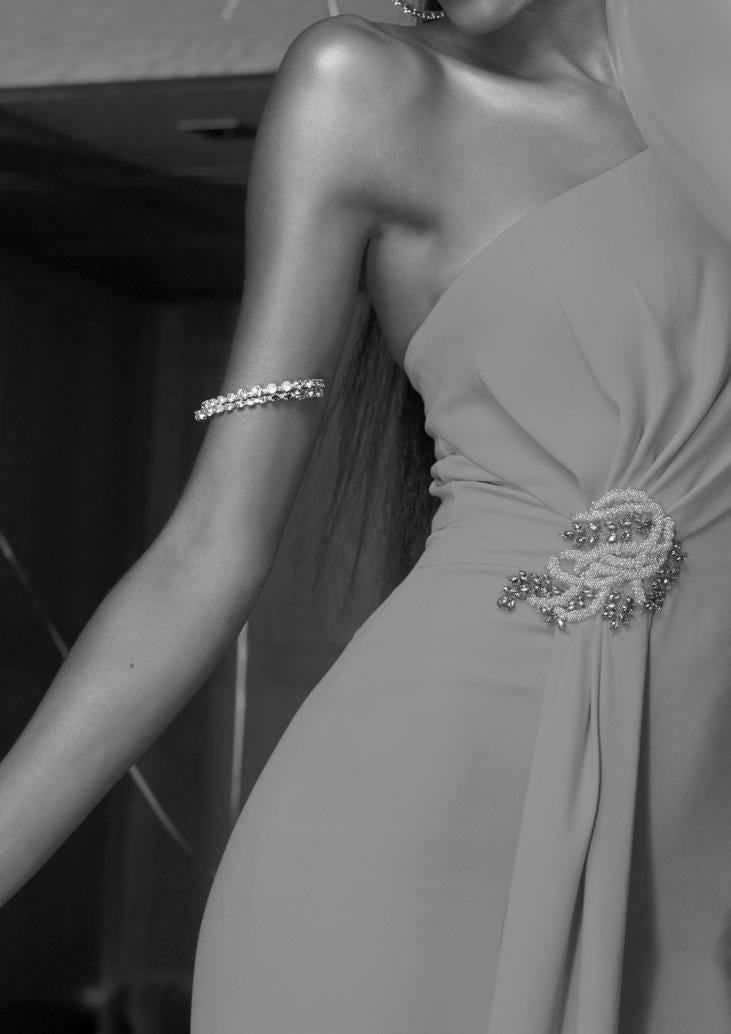 Convidada usando um vestido longo combinado com uma pulseira no braço e um detalhe de broche