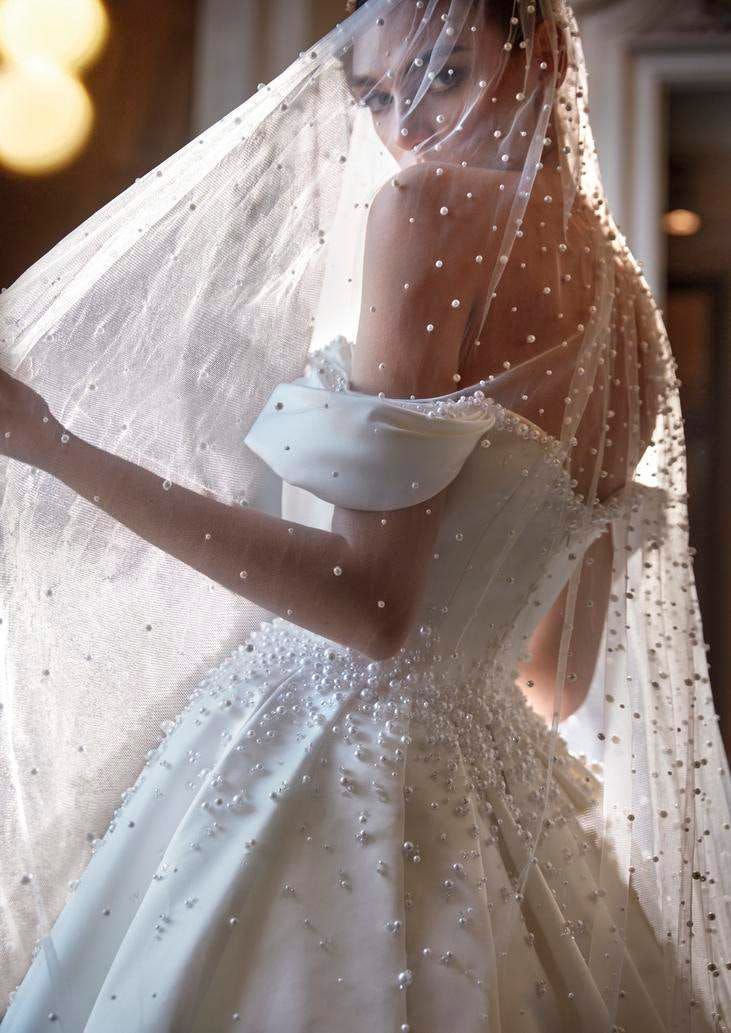 Modella che indossa un abito da sposa principesco con spalline cadenti e lungo velo decorato con eleganti perle.