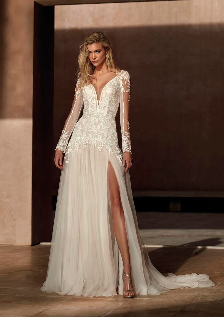 Blonde woman in long-sleeved wedding dress with a slit and lace detailing lining the sleeves