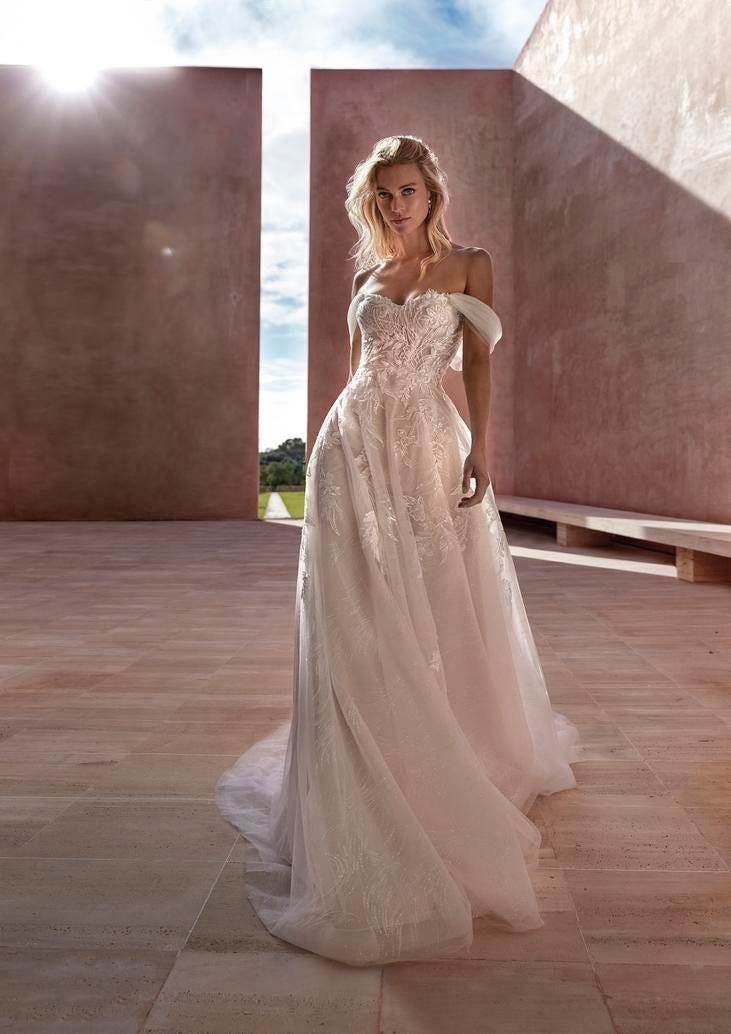 Une robe de mariée bustier aux manches drapées, ornée de motifs en dentelle et d'une longue jupe ample et somptueuse.