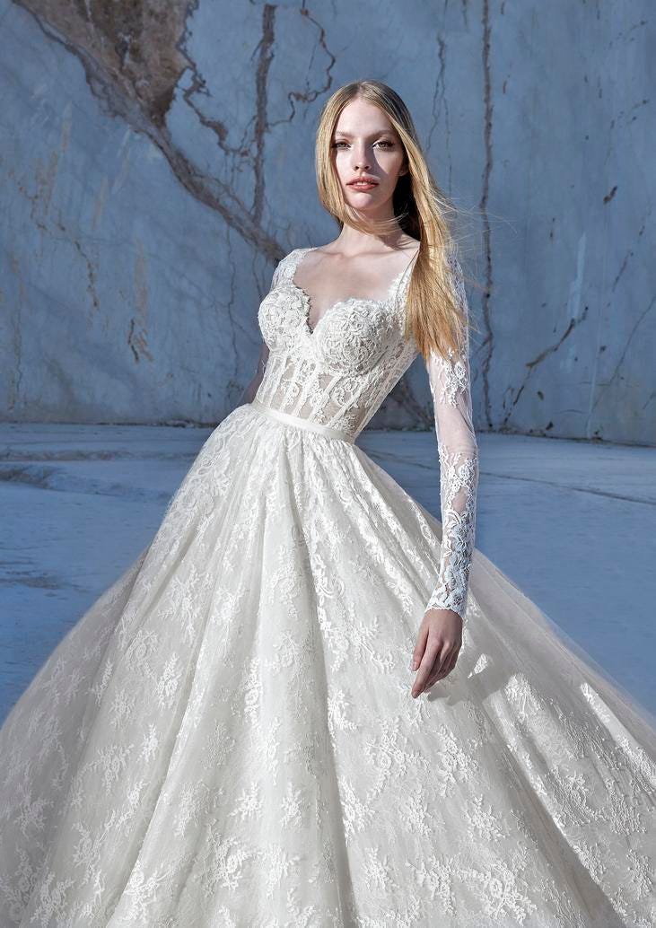Blonde wearing a lace princess wedding gown with sweetheart neckline and delicate long sleeves, standing outside