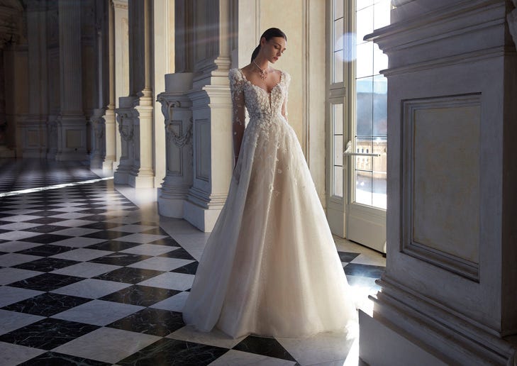 Braunhaarige Braut in weißem Brautkleid aus Tüll mit Spitzenverzierungen in Schlossflur mit karriertem Fliesenboden