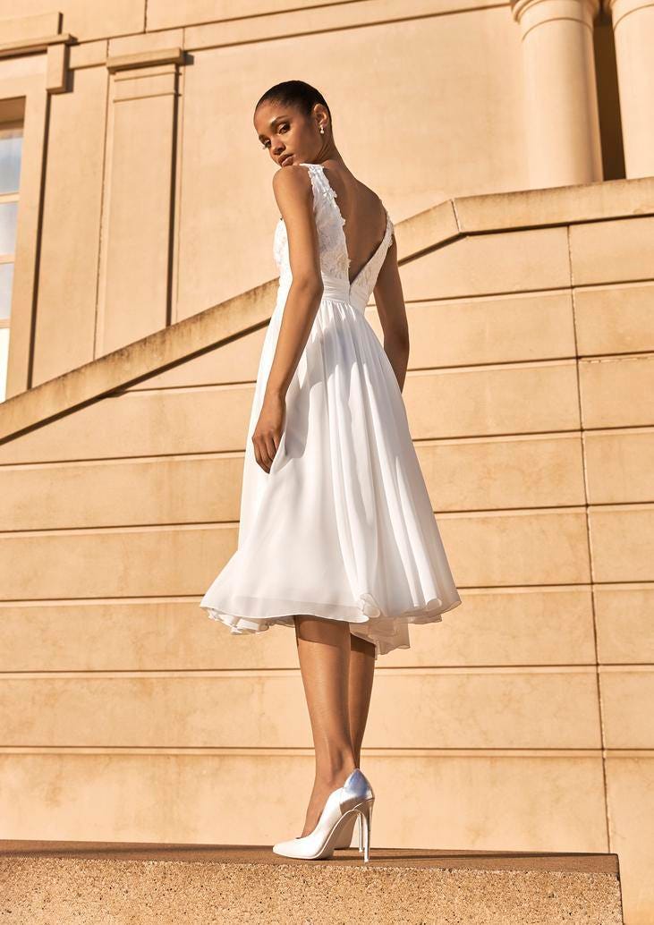 Kobieta w sukni ślubnej do połowy łydki, eksponująca białe buty ślubne na wysokim obcasie