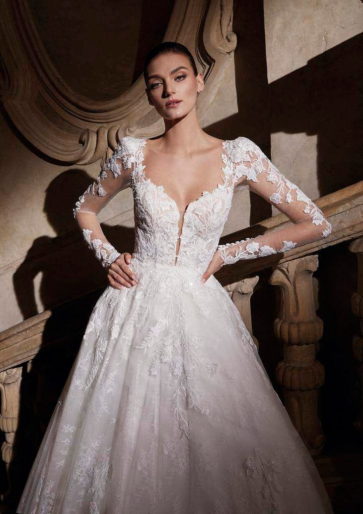 Mujer con las manos en las caderas luciendo un vestido de novia princesa de encaje con una luz tenue
