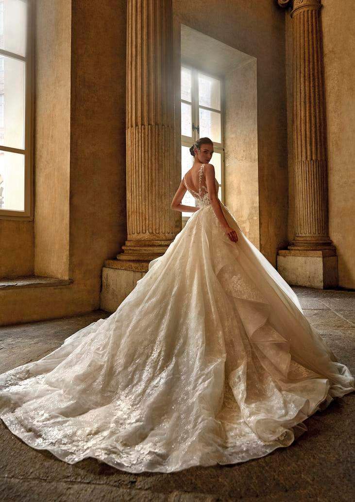 Mujer de espaldas junto a dos columnas altas mirando hacía atrás mientras luce un vestido de novia con corte princesa