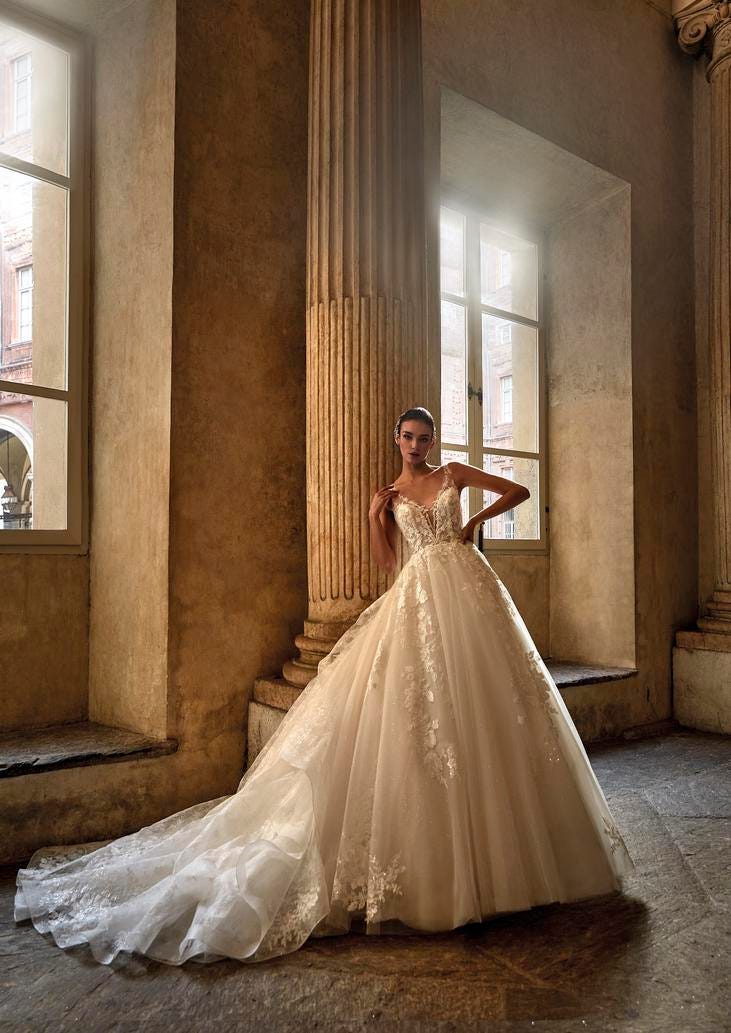 Woman wearing a princess-cut glitter wedding dress with a voluminous ballgown skirt, leaning against a pillar in a building