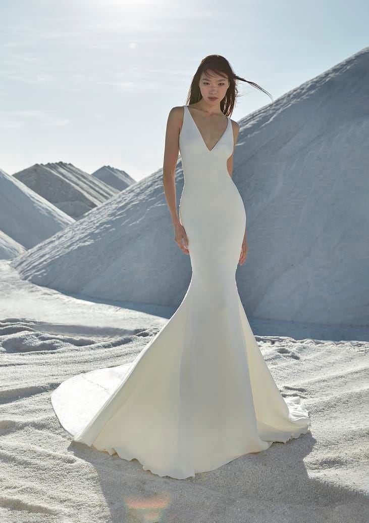 Modella che indossa un abito da sposa bianco, semplice ed elegante a sirena con scollatura a V.