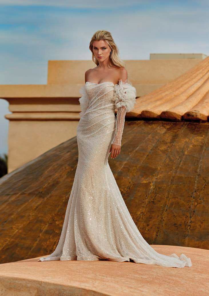 Une mariée vêtue d'une robe de mariée sirène bustier à manches longues tombantes et fleurs à effet 3D.