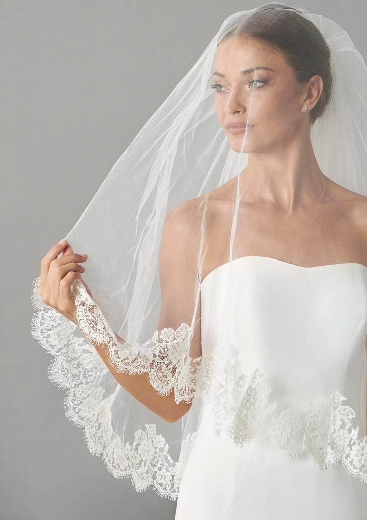 Modella in primo piano che indossa un vestito da sposa semplice e un velo ricamato sul bordo.