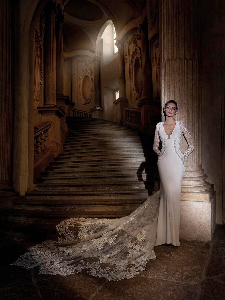 Noiva a posar numa escadaria num vestido estilo sereia de mangas longas com detalhes rendados e transparências