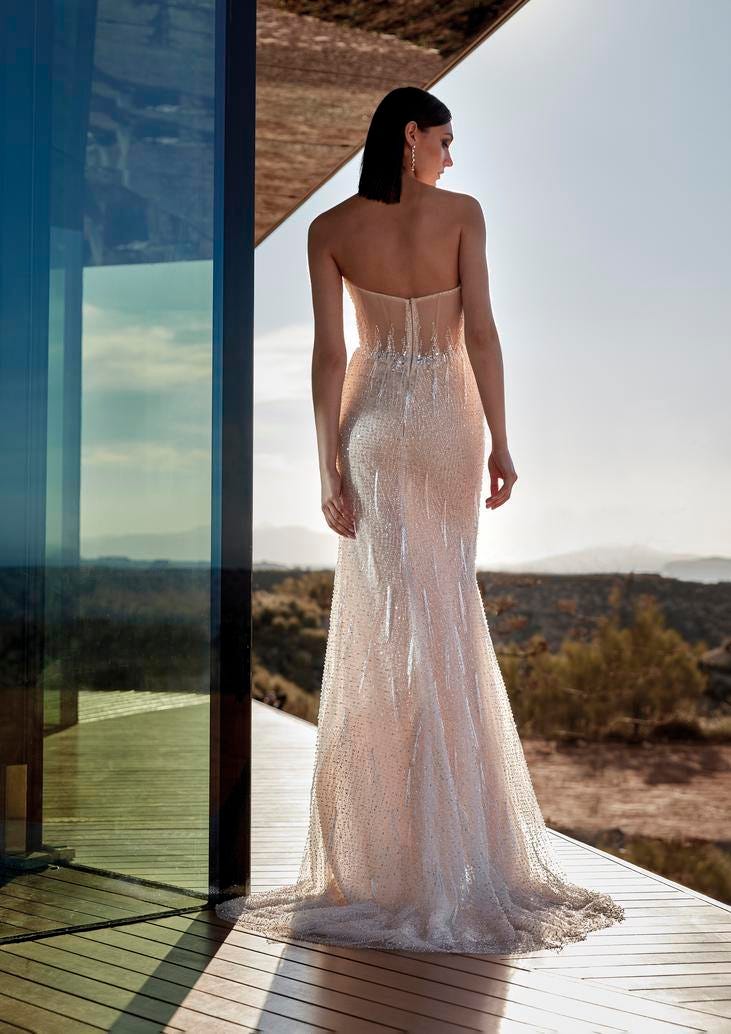 Brunette wearing a sleeveless mermaid wedding dress in beaded tulle with a long skirt, standing outside