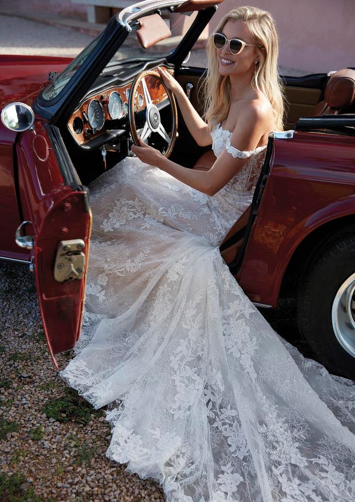 Mujer vestida de novia en el asiento del conductor de un coche retro descapotable con gafas de sol en boda vintage