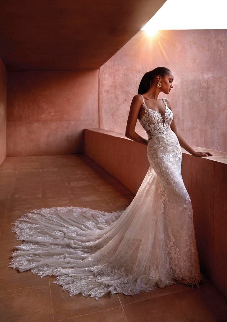 Modella su terrazzo con vestito da sposa in pizzo con strascico, scollo a V e spalline sottili