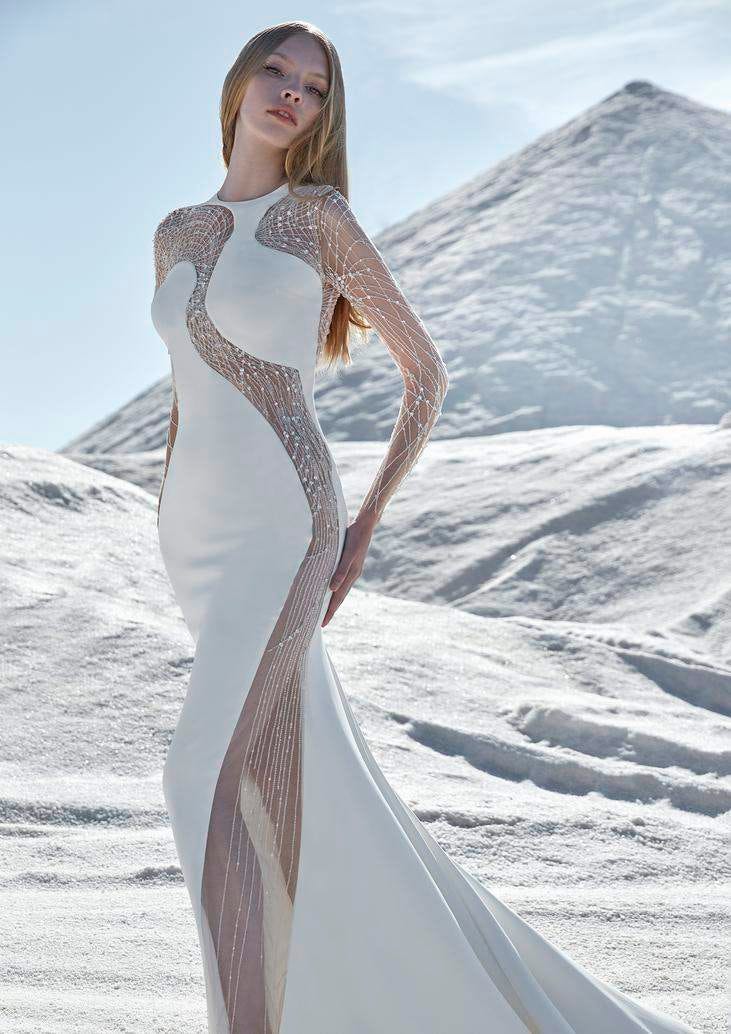 Mujer con un vestido de novia sirena con transparencias en las mangas y por el cuerpo. Al fondo una montaña nevada