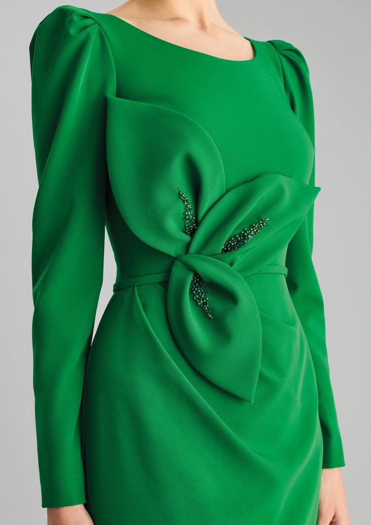 Primo piano di un abito elegante per la mamma della sposa verde con maniche lunghe decorato in vita.