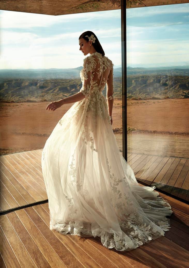 Mujer de pefil con un vestido de novia con transparencias y un tocado para pelo suelto y al fondo las montañas y el cielo